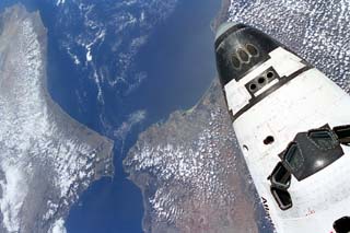 View of the space shuttle Atlantis, STS-71 mission, with a cloudy earth as a background. The payload bay is open as Atlantis makes preparations to dock with the Mir space station.